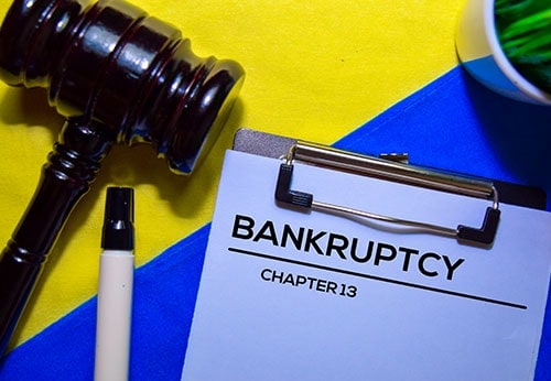 Gavel, marker, and clipboard with 'Bankruptcy Chapter 13' written on paper, set on a colorful background.