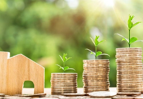 Wooden house model and stacks of coins with growing plants, highlighting key considerations to prevent bankruptcy.