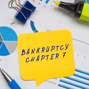 Yellow sticky note with 'Bankruptcy Chapter 7' on documents showing financial charts and graphs.